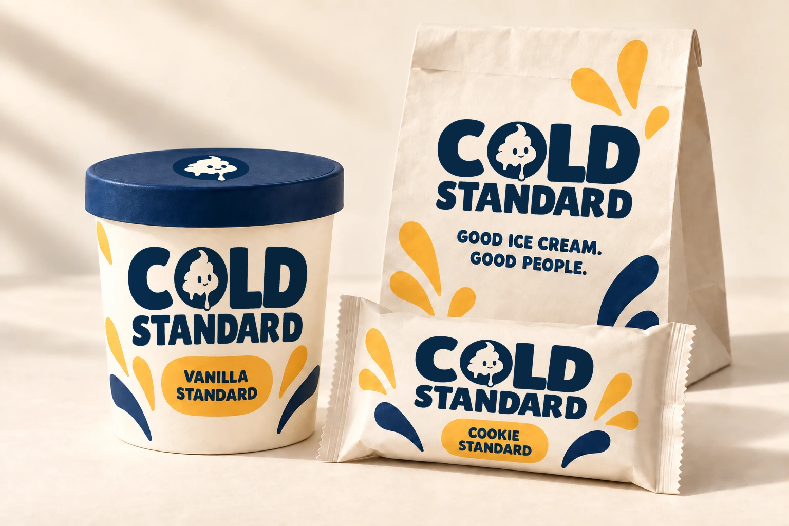 Concept visualization of the Cold Standard packaging family: a cream Vanilla Standard pint with a navy lid, a cream takeaway bag reading Good ice cream. Good people., and a Cookie Standard sandwich wrapper, each carrying the navy Cold Standard logo and yellow drip shapes.